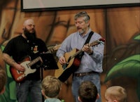 two men playing guitar in front of a group of children