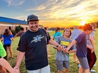 a group of people holding hands in a field at sunset